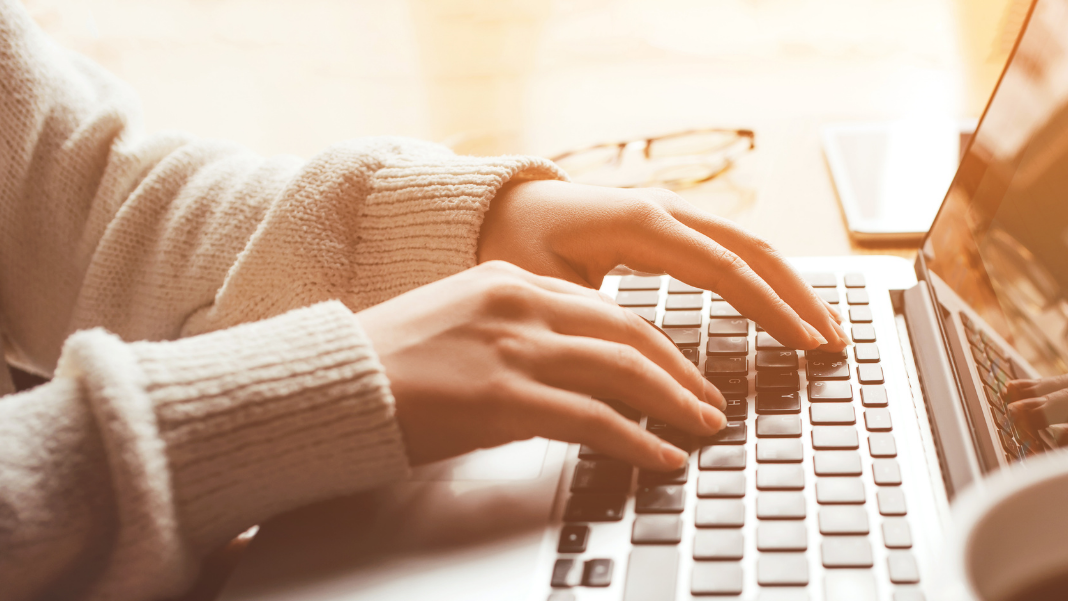 A close up of a woman wearing a cream jumper typing on the keyboard of a laptop